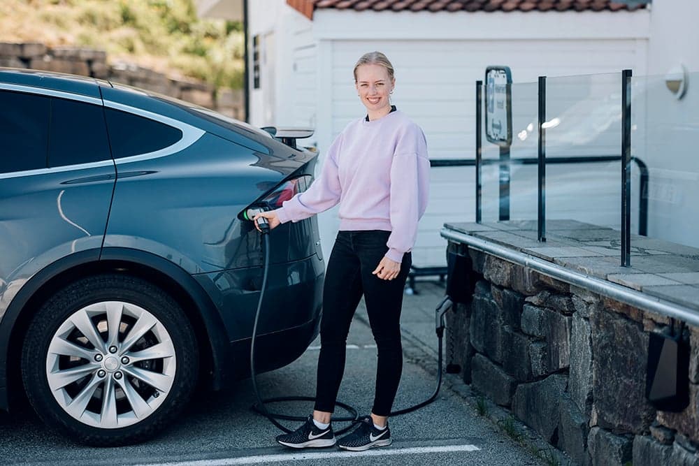 En kvinne i rosa genser lader den grå bilen sin