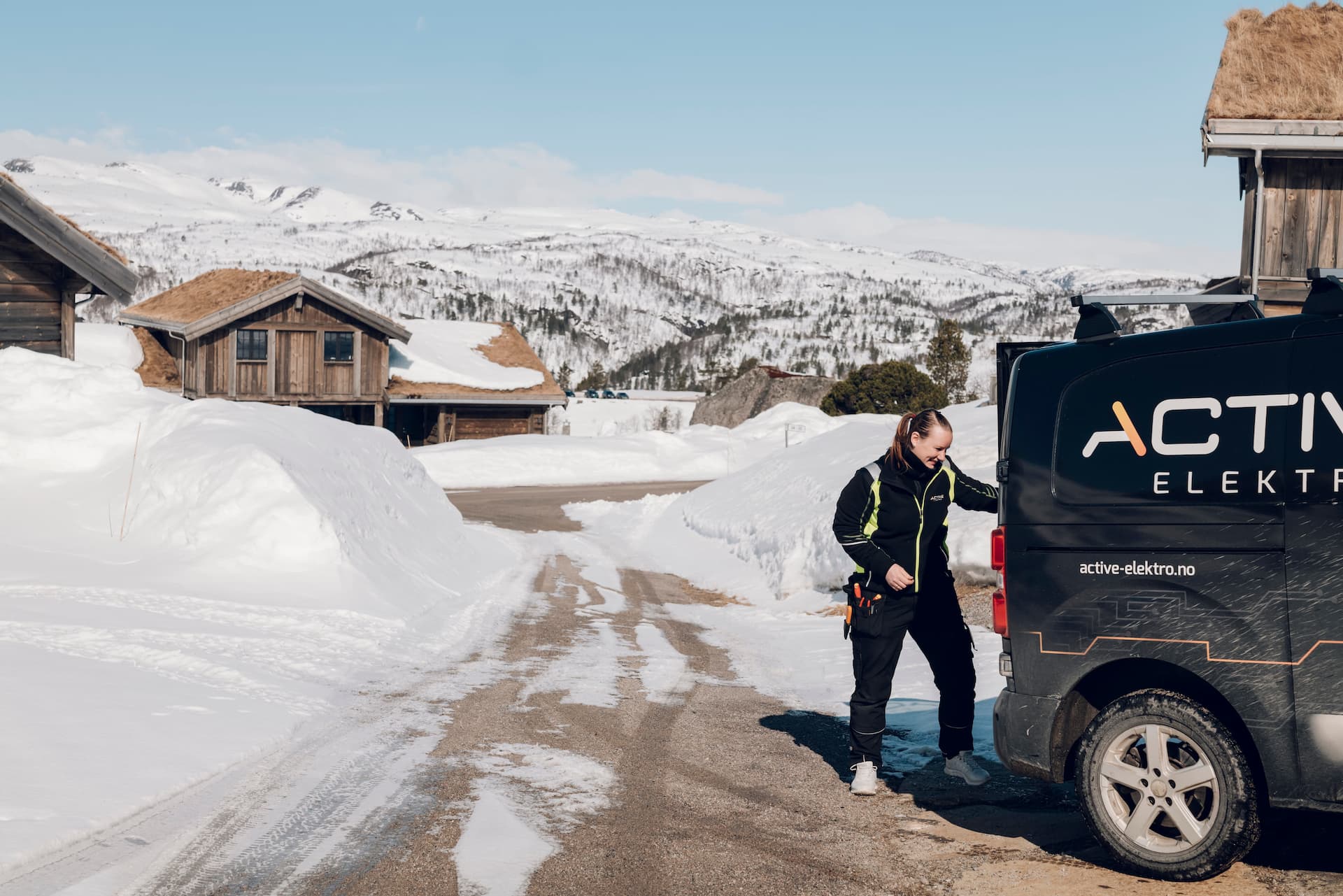 Elektriker Trine Tjørhom står bak bilen sin i et snødekt hytteområde.