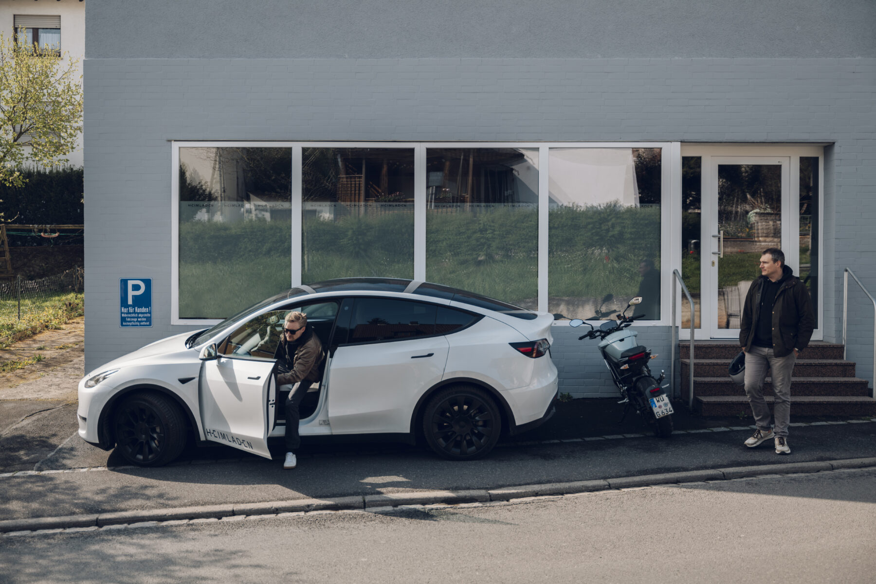 Ein weißer Heimladen-Tesla vor einem Bürogebäude