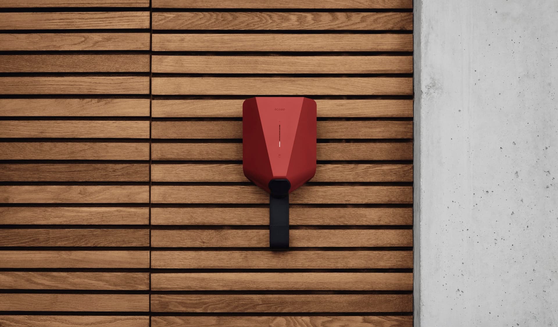 A red Easee EV charger mounted on a wooden wall with a Easee Mount underneath