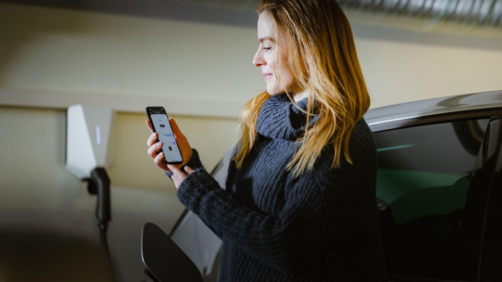Donna che guarda la sua app Easee con il caricabatterie per auto elettriche sullo sfondo