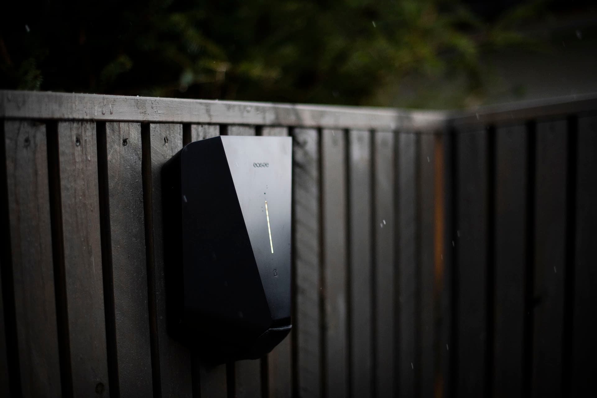 En svart elbillader er installert på et tregjerde