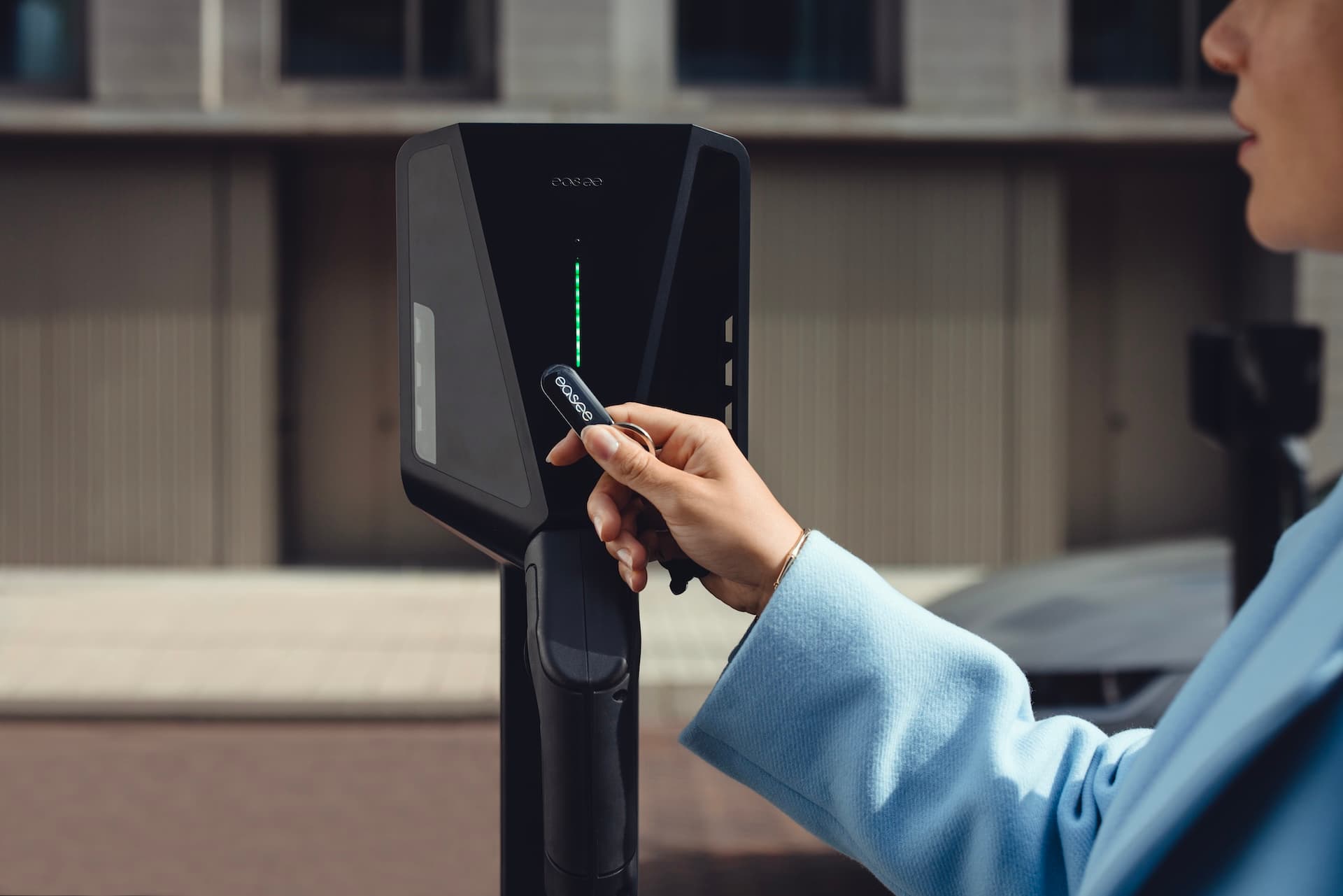 Vrouw houdt RFID-tag tegen zwarte laadpaal voor elektrische auto's