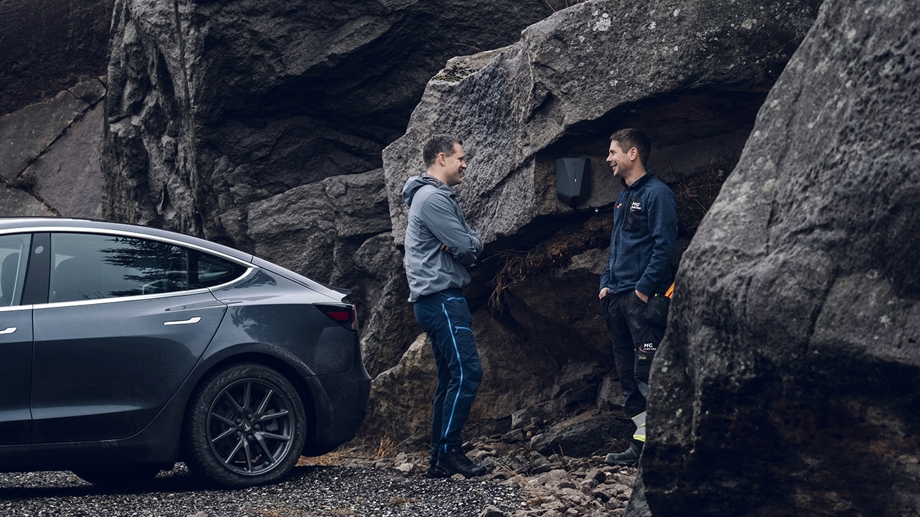 To menn står ved siden av lader og Tesla