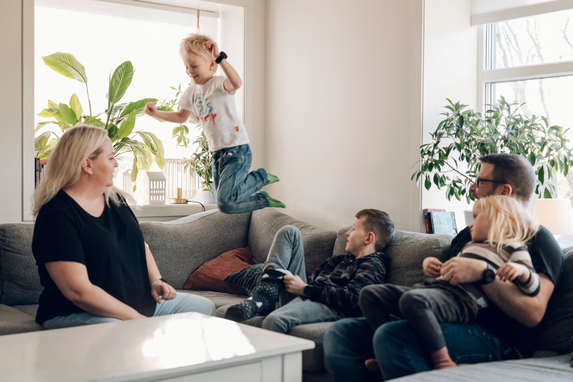 Mor, far og tre barn i sofaen hjemme i stuen.