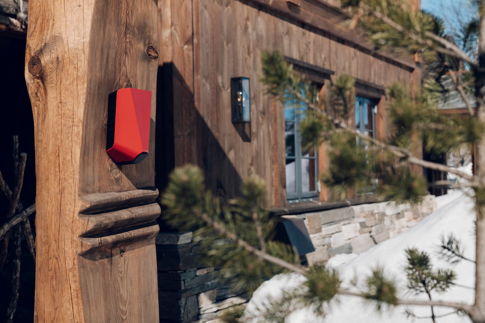 En rød elbillader på et trehus i snøen.