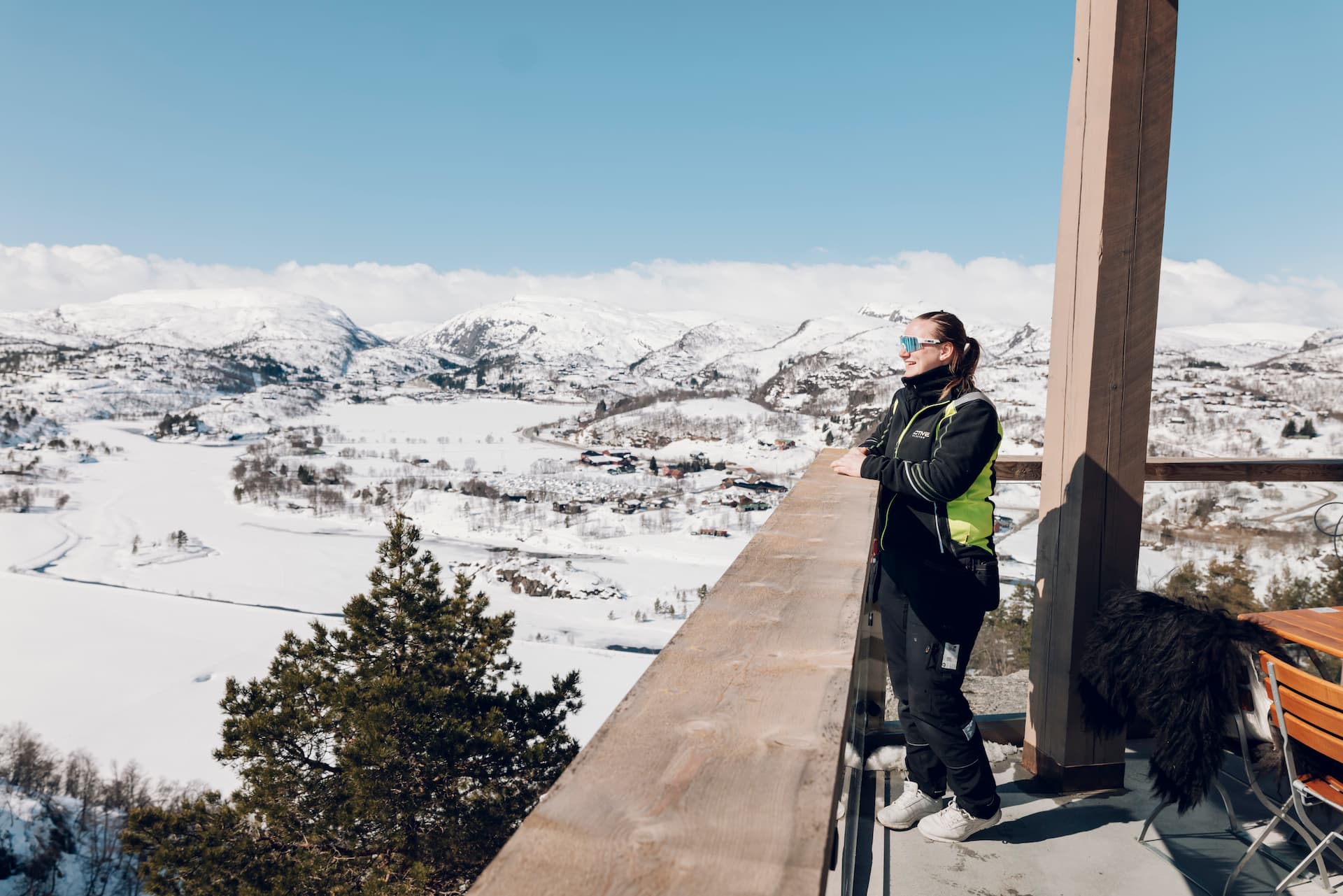 Elektriker Trine Tjørhom nyter solen på en balkong i et snødekt hytteområde.