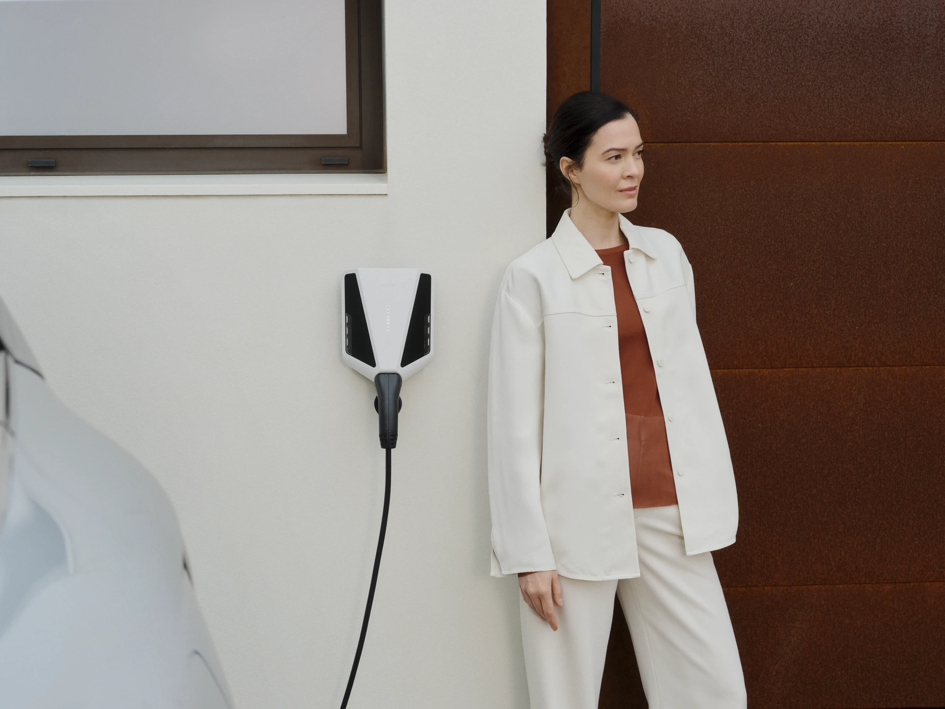 Woman standing beside a wall-mounted Easee EV charger charging an electric car.